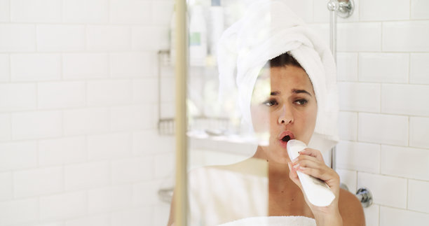 女人在浴室里对着瓶子唱歌，进行头发护理和毛巾护发，在家中梳洗。女孩在公寓里进行日常的清洁和洗发，像唱卡拉OK一样放声歌唱，享受晨间时光。图片下载