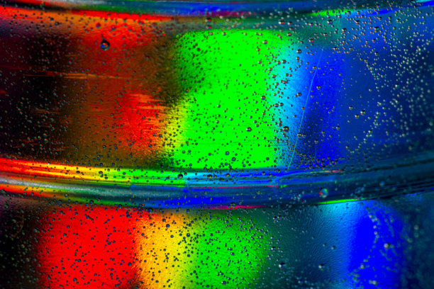 抽象特写照片，展示绿色、橙色和蓝色调的彩色光线反射，带有无数小水滴图片下载