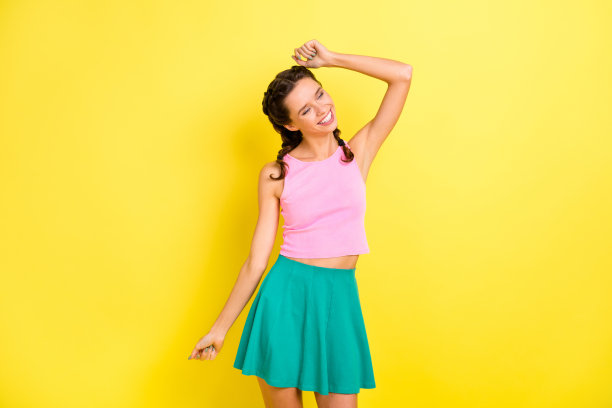 照片：可爱的闪亮少女辫子，穿着背心，闭着眼睛，在孤立的黄色背景上跳舞图片下载