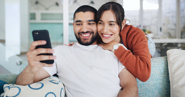 居家自拍的微笑情侣，象征着爱情、关怀，或用于社交媒体分享情侣关系。照片中，一男一女在客厅拍摄个人资料照片，放松地拥抱伴侣，共同珍藏美好回忆。图片下载