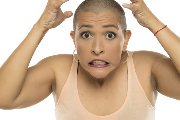 白色背景下，身穿浅色背心的光头焦虑女子双手抱头的棚拍照片。图片下载