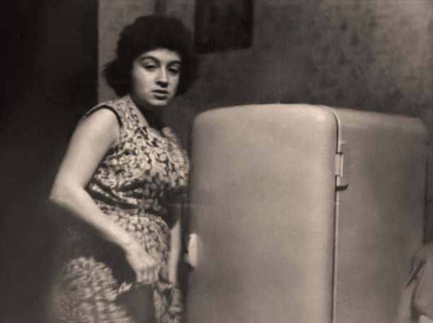 一位美丽的年轻女子站在新买的冰箱旁的复古肖像照。在苏联，人们常与新购买的大件物品合影留念。1961年的复古照片。图片下载