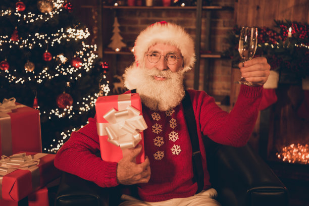 照片：退休老人，圣诞老人，手持香槟礼物盒，在北极屋内圣诞节场景图片下载