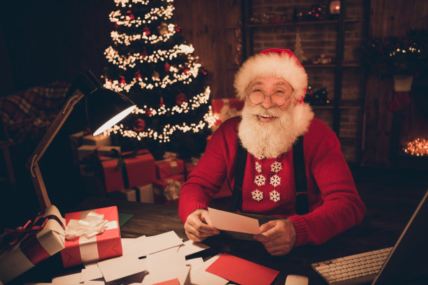 照片：慈祥的圣诞老人室内阅读信件，面带喜悦的微笑，期盼着奇迹、欢乐的圣诞新年。室内光照。图片下载