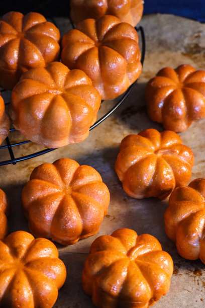 一张在舒适的烘焙坊里，冷却架上摆放着新鲜出炉的自制南瓜面包和万圣节主题面包卷的图片。图片下载