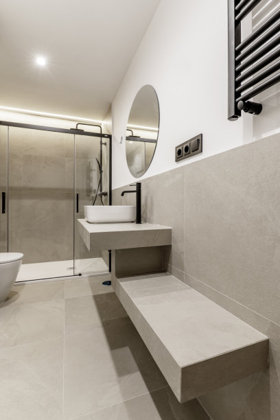 装饰精美的现代浴室，带有灰色瓷砖、同材质台面、圆形镜子、玻璃淋浴隔间、壁挂式毛巾散热器和黑色水龙头。图片下载