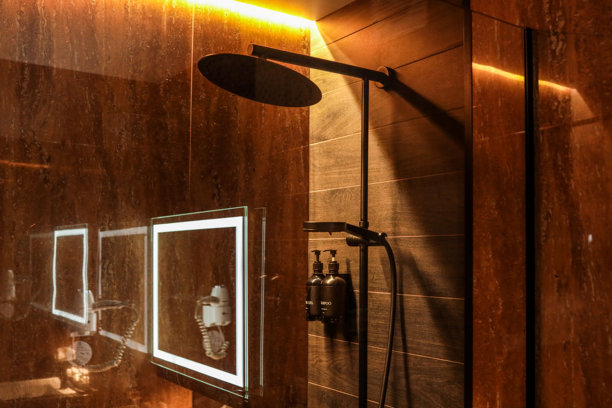现代酒店淋浴间，黑色雨淋花洒，洗发水和沐浴露瓶子在深色瓷砖墙上。豪华浴室配有柔和灯光和镜面反射。图片下载