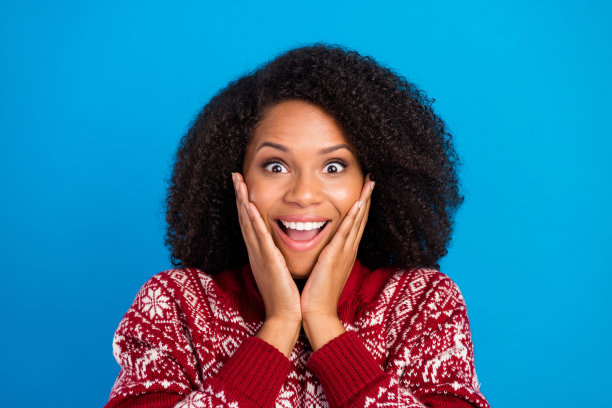 照片：年轻的非洲裔女孩，脸上带着惊讶、惊叹的表情，双手触摸脸颊，信息孤立在蓝色背景上。图片下载