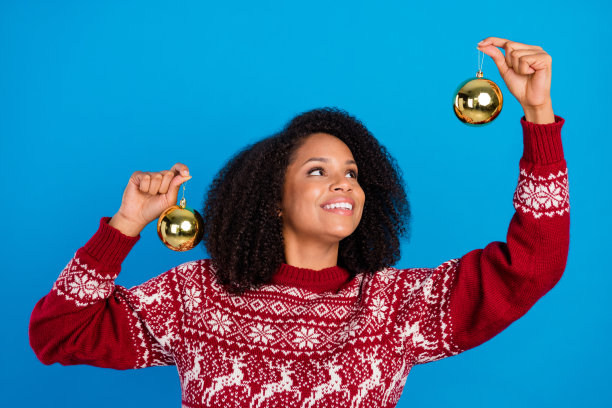 照片，一位可爱、梦幻的女士，穿着印花套头衫，手持装饰球，望着远方，面带微笑，在孤立的蓝色背景前。图片下载