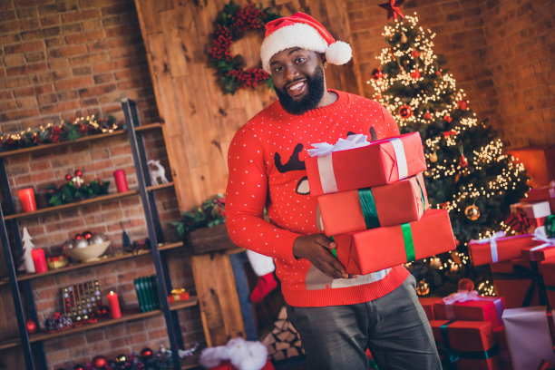照片：一个开心的非裔美国年轻男子在室内家中拿着礼品盒，庆祝圣诞节。图片下载