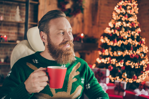照片：一个留着胡子的红发男子坐在办公室内，戴着套头衫，手里拿着咖啡杯，看起来好奇而友善。图片下载