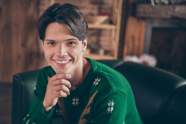 照片，一个迷人、快乐的年轻男子，手托下巴，面带微笑，心情愉悦，室内，圣诞节，房子，家，公寓图片下载