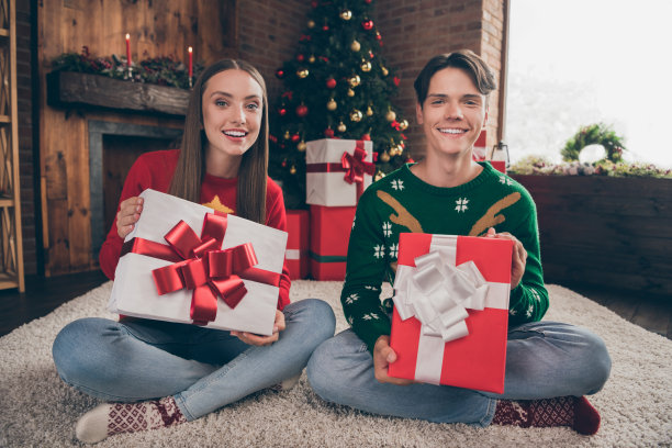 照片中，一对快乐的夫妇坐在地毯上，周围是圣诞礼物，他们在室内家中。图片下载