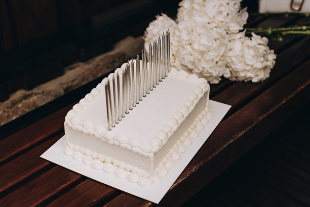 一张在木凳上的白色生日蛋糕图片，上面插着高高的蜡烛，并装饰有鲜花。图片下载