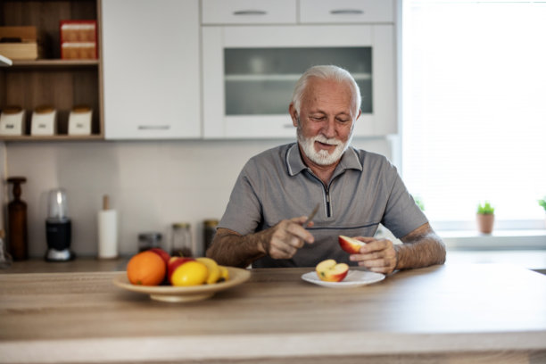 白天在家里吃苹果的微笑男人肖像。一位老人正在吃苹果的照片。图片下载