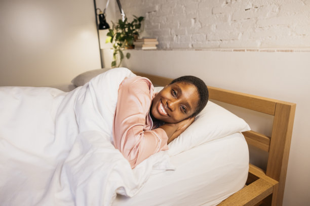 Woman waking up in bed smiling in pajamas图片下载