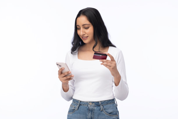 年轻女子在白色背景前使用智能手机和信用卡进行购物的素材照片图片下载