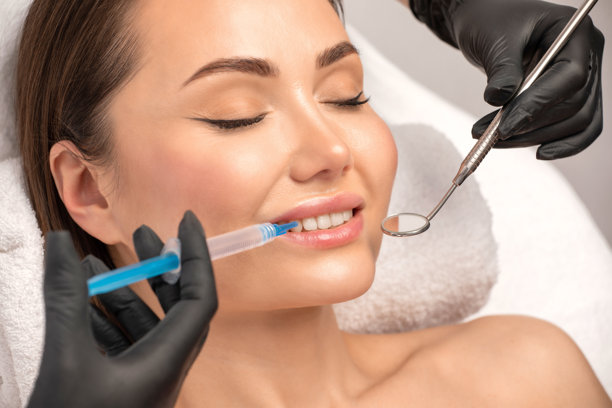 牙医在诊所为一位年轻漂亮的女士进行牙齿美白治疗。健康的笑容。图片下载