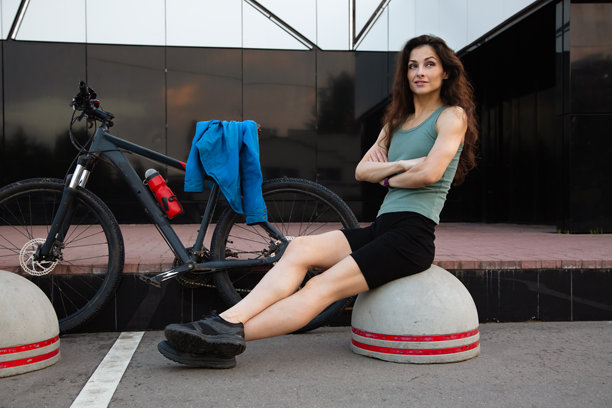 年轻健美的女性穿着运动服，在夏日阳光明媚的街道上，与她的黑色山地自行车坐在一起休息。户外运动锻炼。图片下载
