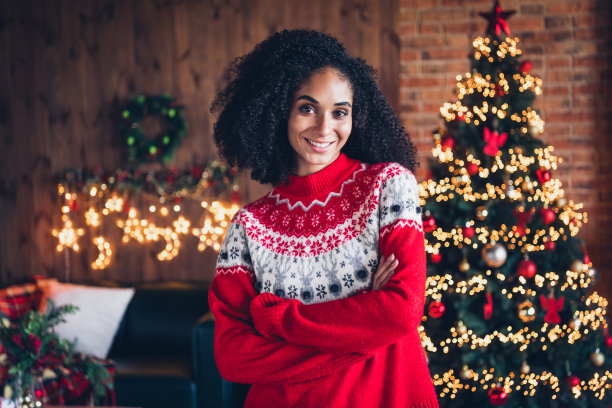 照片：一位漂亮的、积极的女士双手交叉，在一个室内房屋的新年节日常青树花环装饰旁摆姿势。图片下载