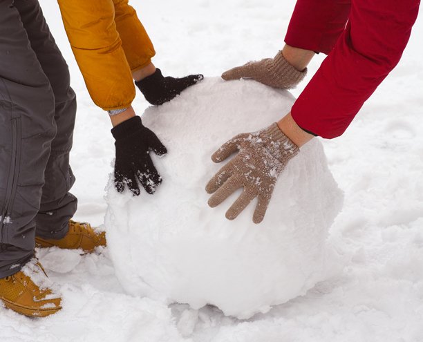 近景：孩子和他的母亲在雪地里推着一个大雪球。图片下载