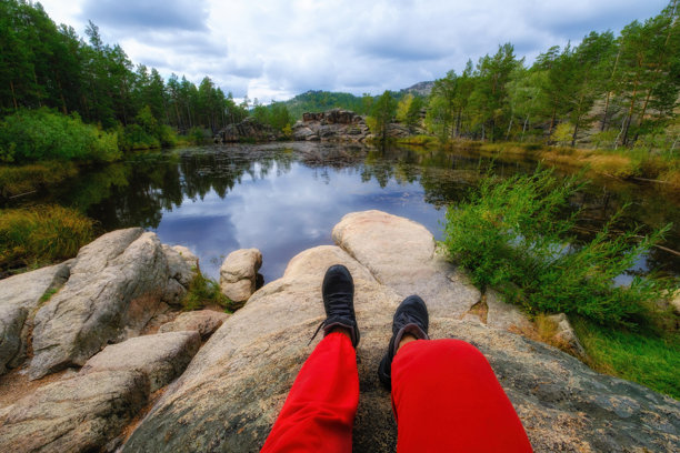 一个人坐在哈萨克斯坦卡尔卡拉利自然公园神秘的Shaitankol湖（又名魔鬼湖）岸边，周围是茂密的松树林和巨大的悬崖。第一人称视角照片图片下载