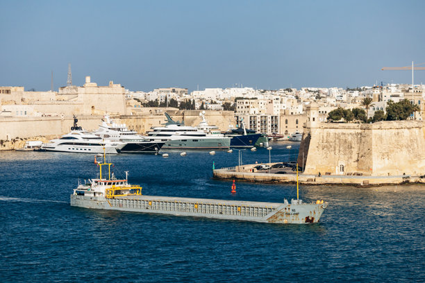 货船驶过大港，经过停泊在历史悠久的石灰石防御工事下的豪华游艇的社论图片图片下载