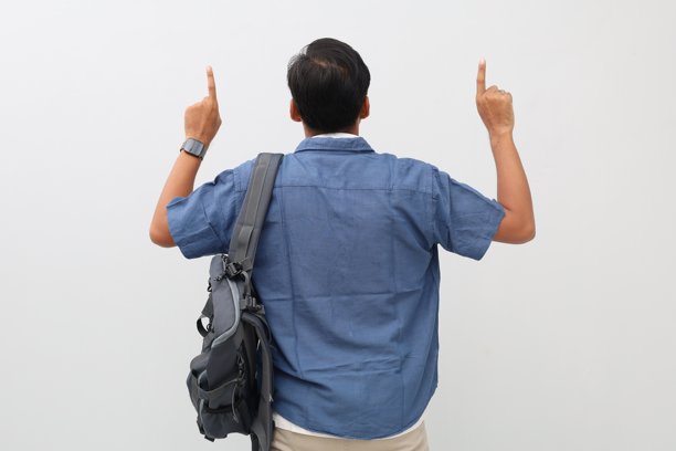 特写照片，年轻男子背影，身穿格子衬衫，背着背包，手持书籍，向上指着，独立于白色背景图片下载