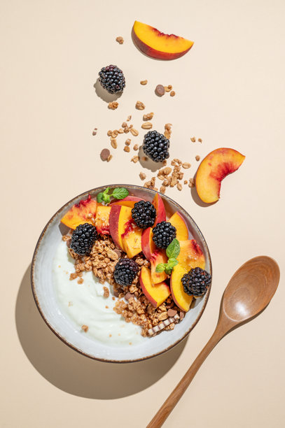 碗里的希腊酸奶，配燕麦格兰诺拉或谷物、桃子和黑莓，背景为米色。图片下载