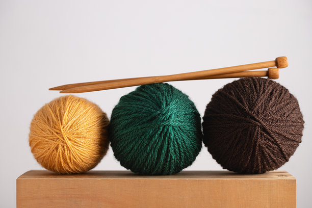 黄、绿、棕色绒线球和编织针放在浅木桌上。简约风格的横幅图片，背景中性。留有复制空间。手工工艺和创意爱好的概念。图片下载