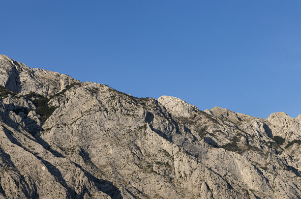 灰色的岩石，长着少量植被，背景是天空。克罗地亚山地风光，可供复制。图片下载