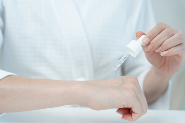 美丽的亚洲女性微笑着测试精华液以获得良好肌肤。健康女性的脸部涂抹面霜和化妆品。皮肤霜、抗皱、娃娃脸、美白、保湿广告。图片下载