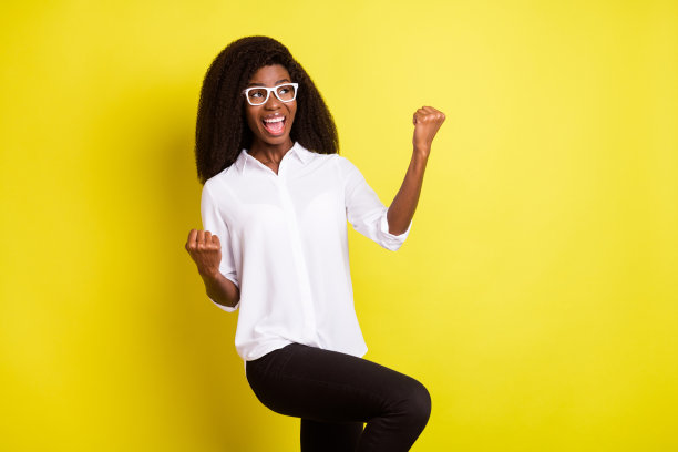 照片肖像：一位戴眼镜、穿白衬衫的年轻女子，她望着复制空间，做出胜利者的手势，背景是充满活力的黄色。图片下载