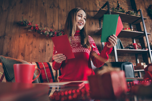 照片：一位穿着红色毛衣的迷人甜美年轻女子在室内房间/家中/房子的新年祝福中带着微笑图片下载