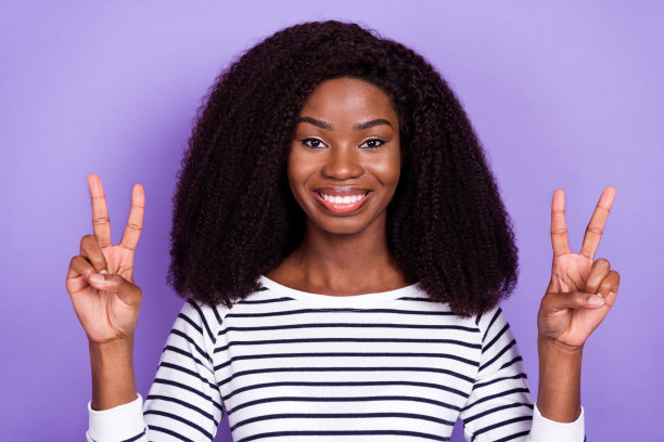 照片：一个快乐、积极微笑的年轻非洲女孩，做出和平的手势，在紫色背景下显得很酷，是隔离的。图片下载