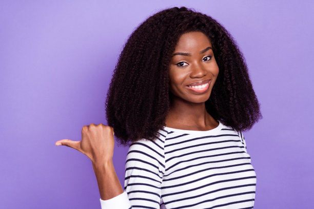 身穿条纹毛衣、激动地指向空白处的年轻女士的个人资料照片，孤立在紫色背景上图片下载