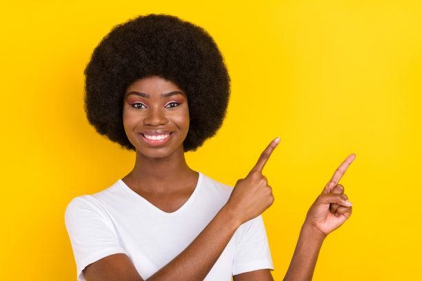 照片：一位快乐、友善、漂亮、深肤色女性，手指着黄色背景上的空白空间，心情愉悦，背景隔离。图片下载