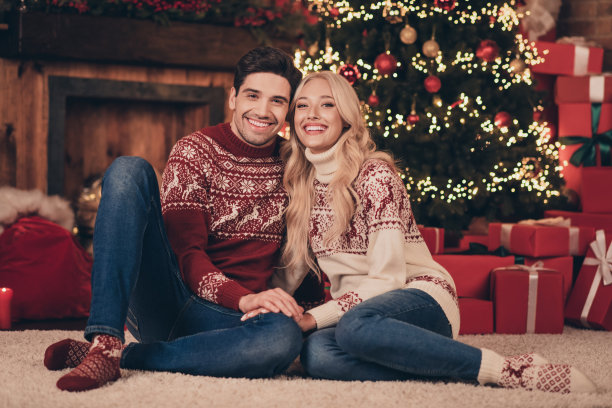 照片：一对穿着印花毛衣的恩爱夫妻，在室内温馨的家中，面带微笑，享受着圣诞时光，互相拥抱。图片下载