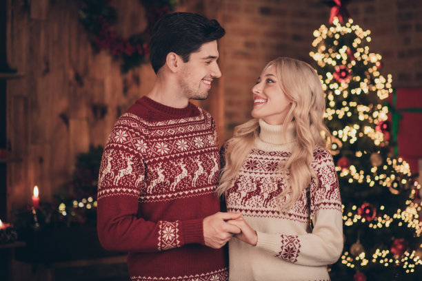 照片：一对有趣的、迷人的夫妇穿着印花毛衣，面带微笑，在室内房屋的房间里拥抱着，享受着新年气氛。图片下载