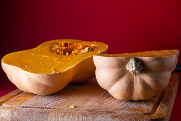 纵向切开的冬南瓜，放在木质砧板上，背景为红色。图片展示了南瓜表皮的详细纹理。图片下载