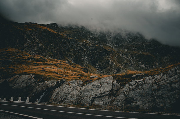乌云密布的戏剧性天空下，穿越崎岖斜坡和浓雾的忧郁山路图片下载