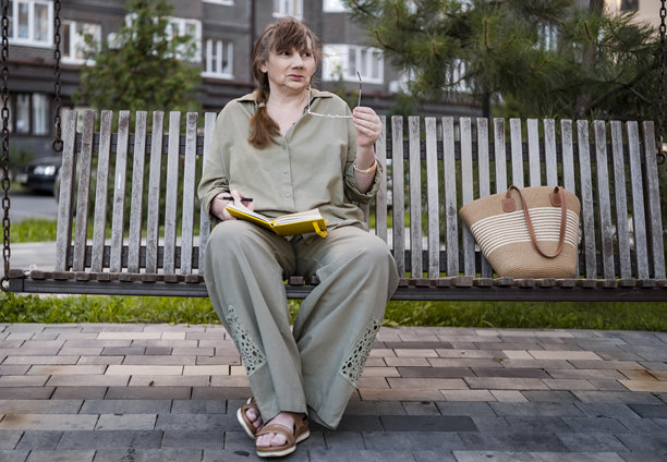 年长女性若有所思地坐在公园里，手绘笔记本，享受爱好。体现了活跃的晚年生活和老年人的创造力。图片下载