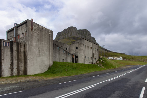 多云天空下，废弃的混凝土工业建筑沿着山路坐落在崎岖的山脊附近。图片下载