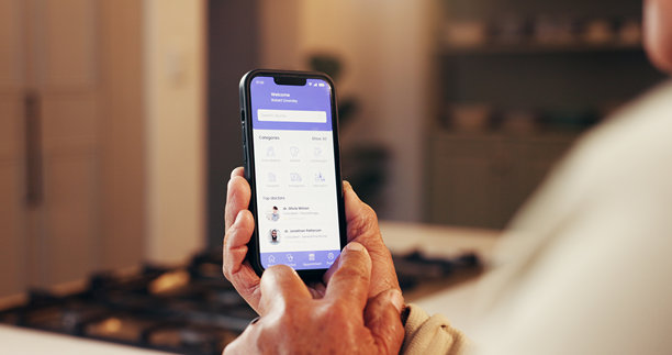 老年人在家中，手持手机屏幕，屏幕上显示着应用程序，用于与医生沟通和进行研究。这位老人正在使用科技产品进行在线浏览和信息查阅，进行远程医疗，为退休生活做准备。图片下载