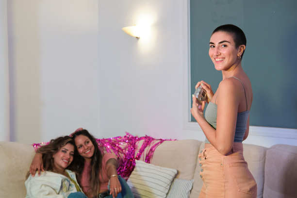 自信的年轻女性朋友们在家庭派对中使用数码相机拍照并在沙发上休息的中景照片图片下载
