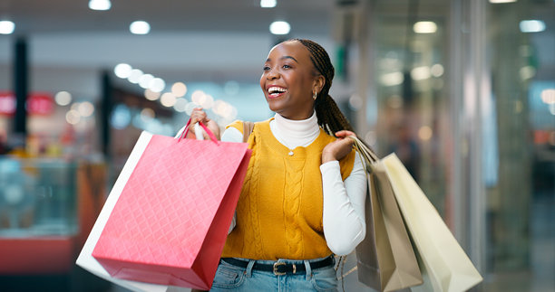 快乐的非洲女性提着购物袋在商场里行走，可能是为了折扣交易、清仓促销或虚化背景。这位顾客是为了时尚促销、黑色星期五或优惠礼品而购买奢侈品牌商品。图片下载