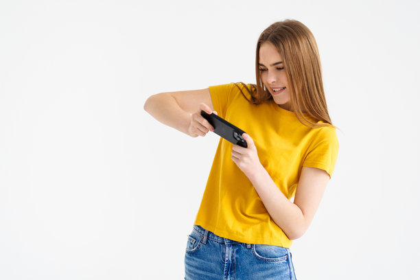 年轻女子在白色墙壁背景前玩手机游戏的照片图片下载