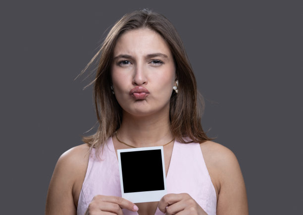 一位快乐的女士眨着眼睛，手里拿着一张空白的即时照片图片下载