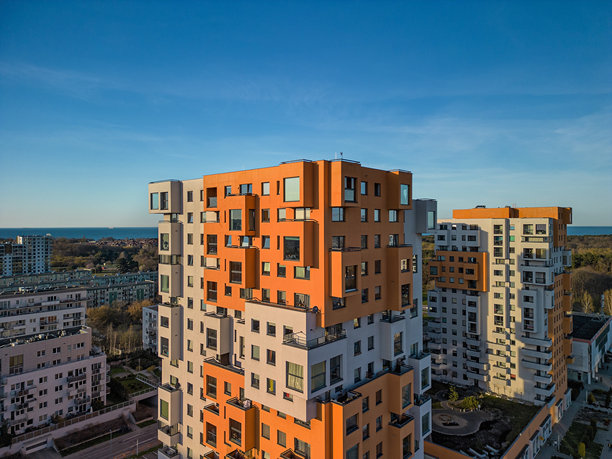 垂直航拍HDR照片，展示了日落时格但斯克Przymorze地区现代的橙白色高层建筑，突出几何立面。图片下载