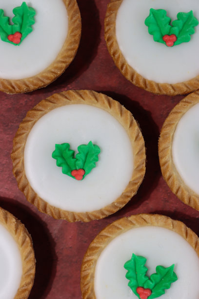 自制圣诞肉馅饼的整张照片，上面覆盖着白色糖霜，装饰着绿色和红色的冬青叶和浆果，节日圣诞甜点酥皮点心配甜肉馅，斑驳的红色背景，俯视平铺，高视角图片下载
